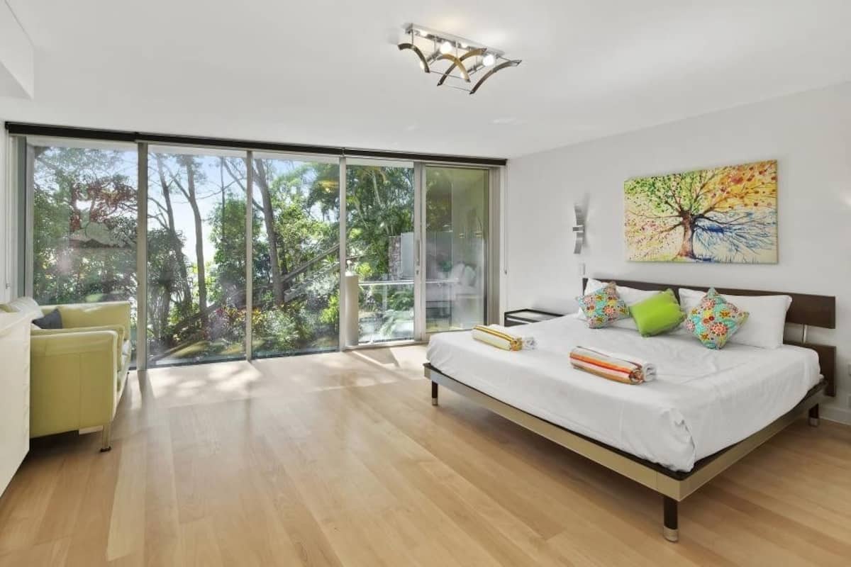 A modern bedroom with a large bed, a view through a sliding glass door, and a ceiling light fixture.