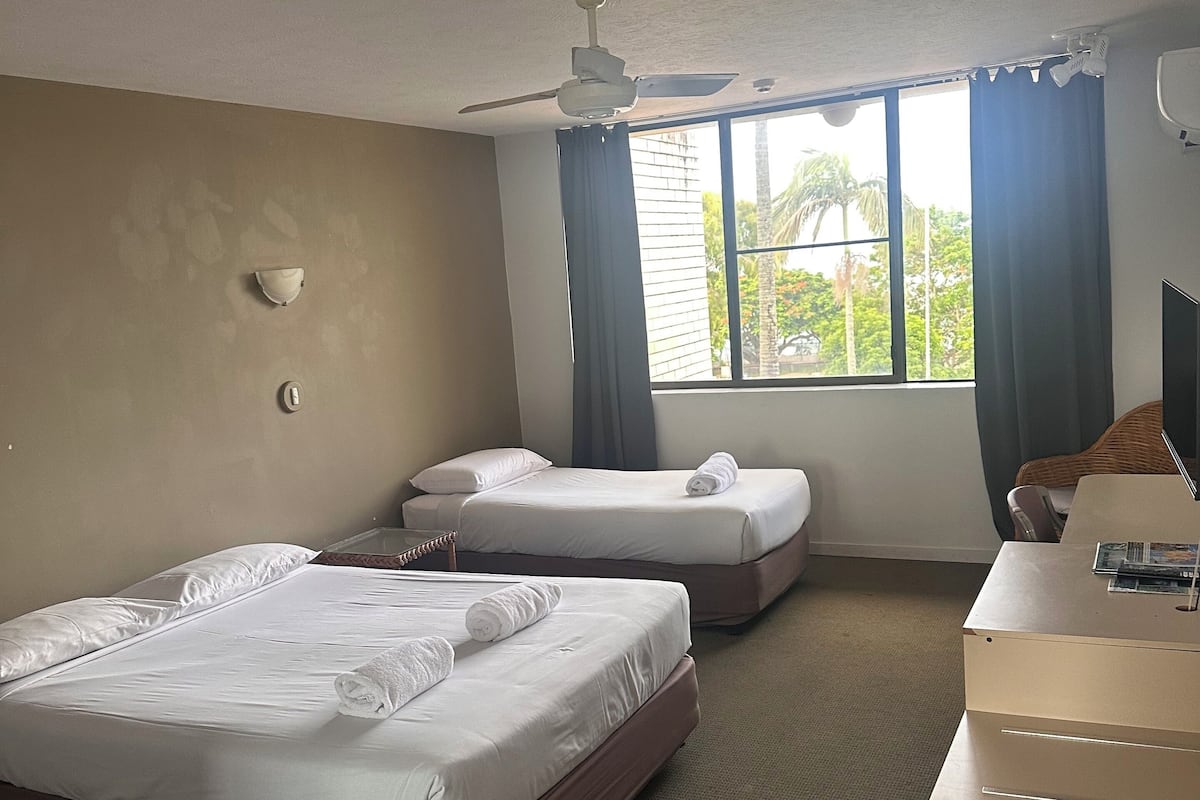 Une chambre d’hôtel avec deux lits, un bureau, un ventilateur de plafond et une fenêtre avec des rideaux.