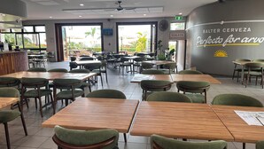 A spacious restaurant with multiple tables and chairs, a bar area, and a wall with a sign for toilets. - Hervey Bay Hotel & Resort (Pialba)