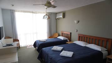 A hotel room with two beds, a desk, a chair, a ceiling fan, and a window with curtains.