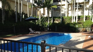 A swimming pool with a metal fence, surrounded by a brick patio and greenery. - Hervey Bay Hotel & Resort (Pialba)