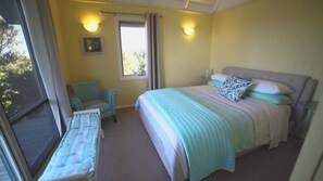 A bedroom with a bed, a chair, a window, and a bedside table.