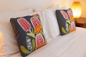 A bed with white linens and two decorative pillows with a floral pattern.