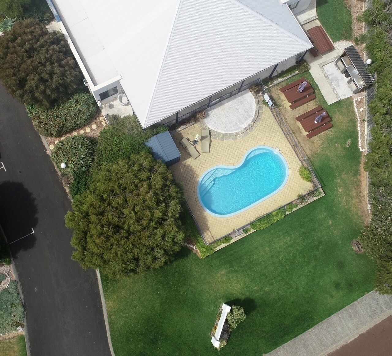 An aerial view of a residential property with a swimming pool, a covered patio, and a lawn.