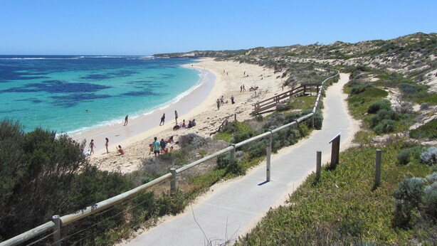 A coastal road with a beach on the right, a clear blue sky, and a few people on the beach. - Surfpoint Resort (Gnarabup)