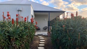 A pathway leading to a modern building with a covered entrance, surrounded by lush greenery and red flowers. - Surfpoint Resort (Gnarabup)
