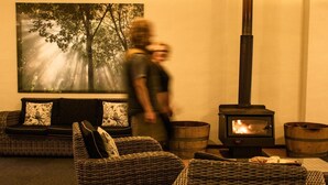 A cozy living room with wicker furniture, a fireplace, and a large window with a forest view. - Surfpoint Resort (Gnarabup)