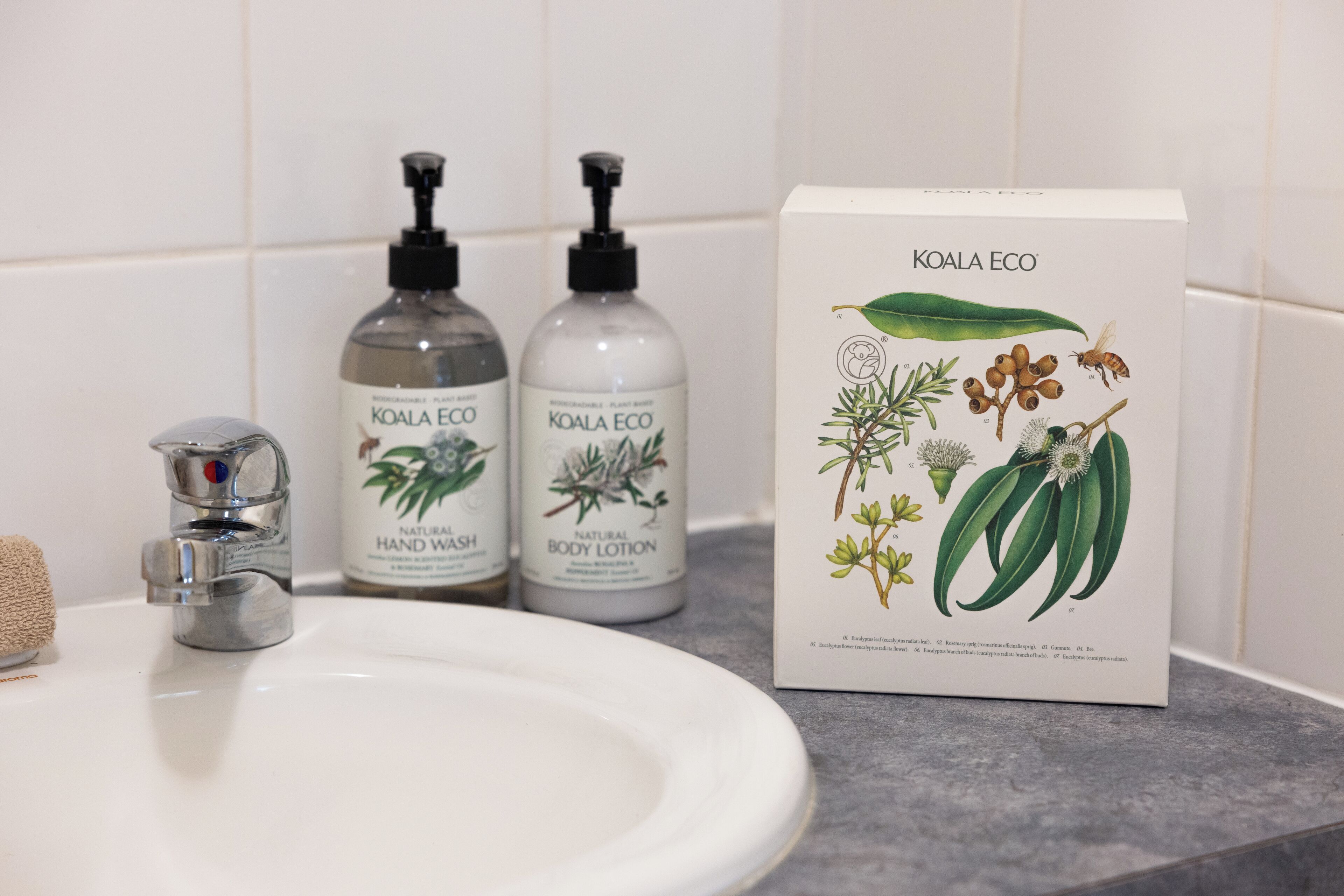 Un lavamanos con dos botellas de Koala Eco para lavado de manos y loción corporal, y una caja con ilustraciones botánicas.