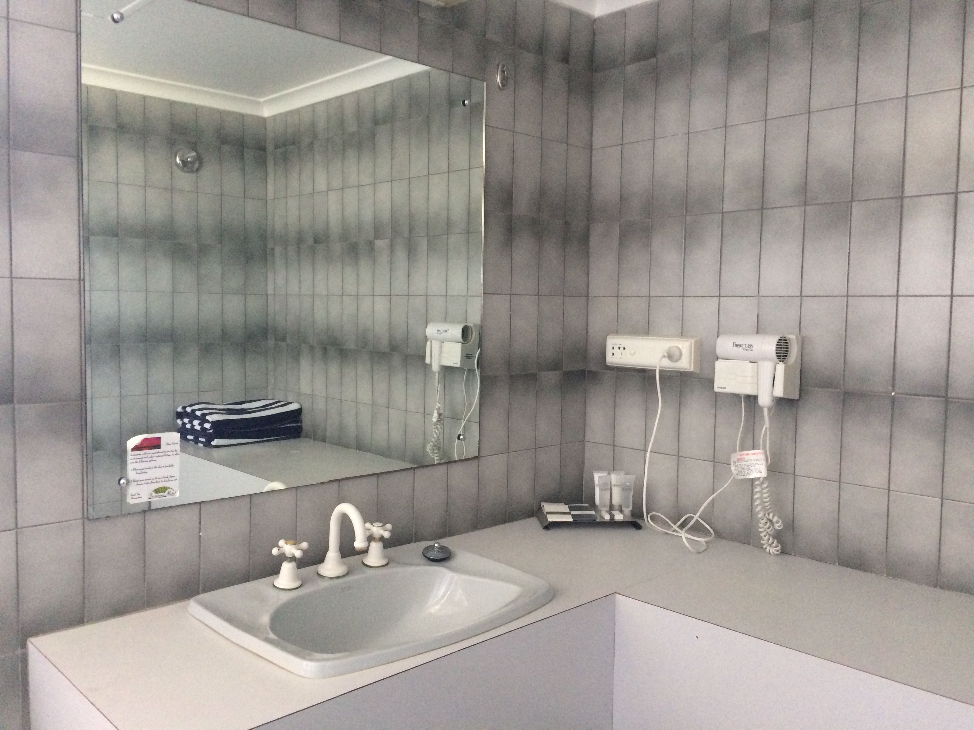 A bathroom with a large mirror, a sink with two faucets, and two hair dryers mounted on the wall.