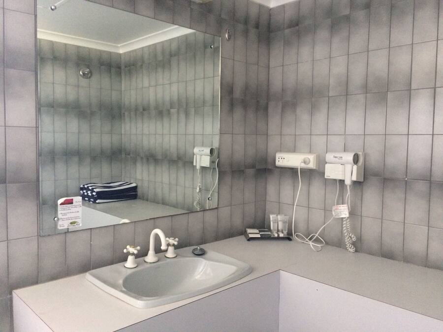 A bathroom with a large mirror, a sink with two faucets, and two hair dryers mounted on the wall.