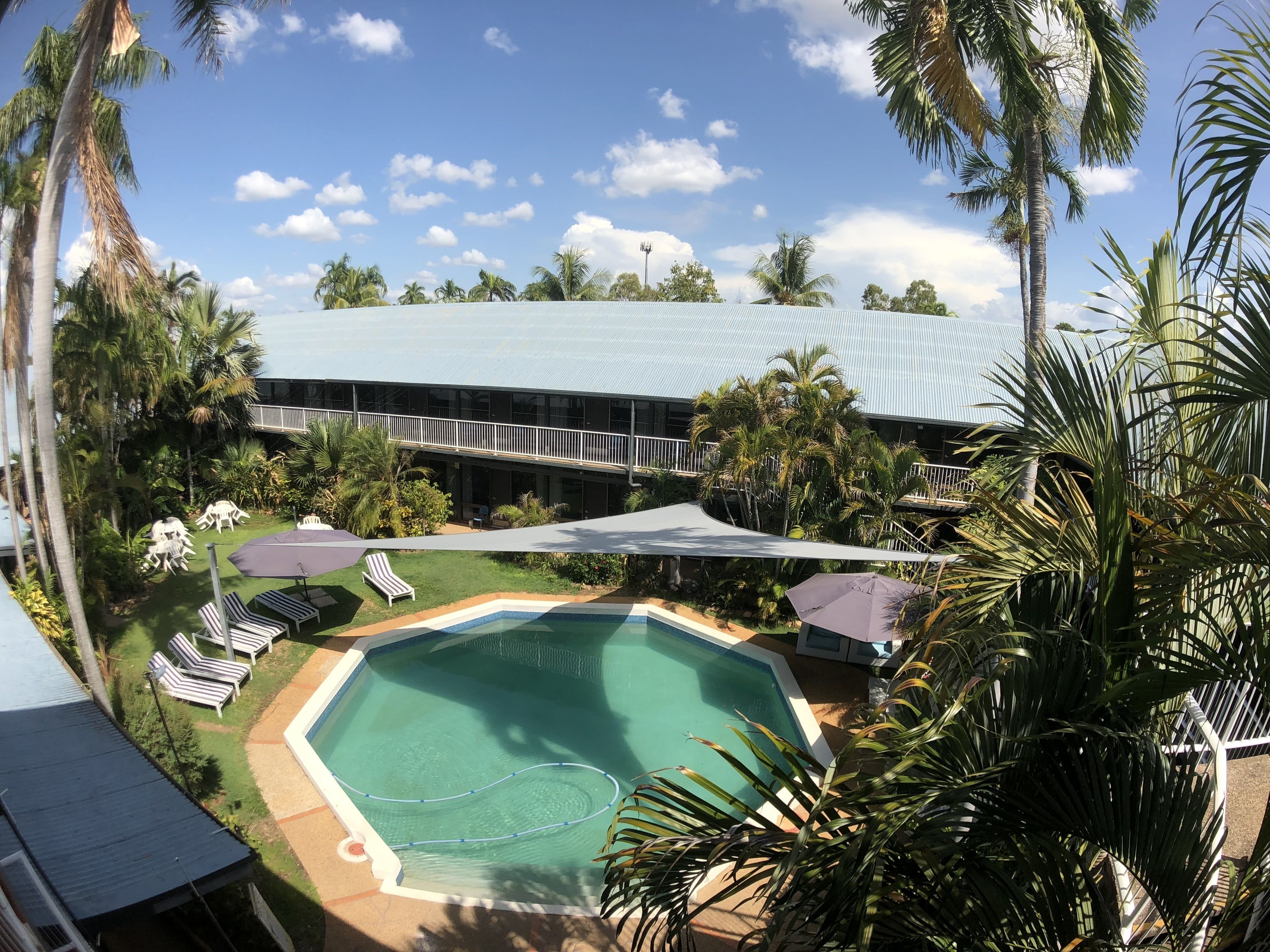 A pool area with lounge chairs, a covered seating area, and a building with a blue roof.