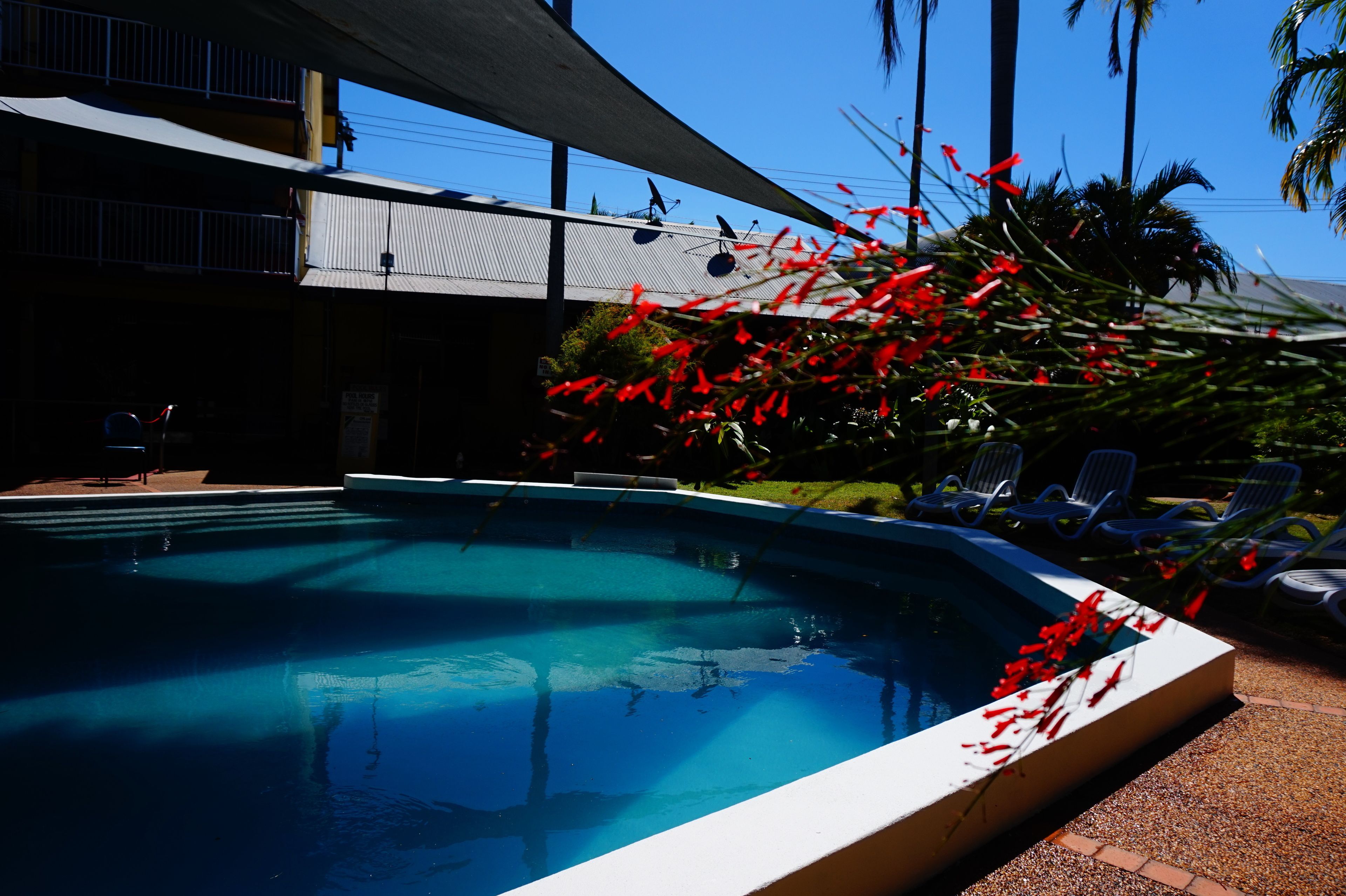 A swimming pool with clear blue water, surrounded by lounge chairs and a building with a balcony.