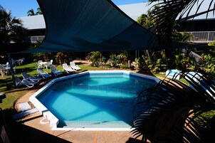 Una piscina con sillones de descanso y una zona sombreada.