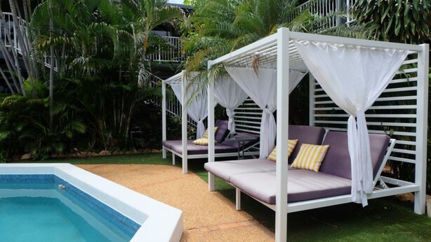 Un espace aménagé au bord de la piscine, comprenant deux lits à baldaquin blancs, une piscine et une végétation luxuriante.