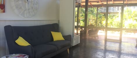 A dark grey sofa with two yellow cushions, a small round table with magazines, and a large wall clock.