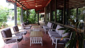 Un espace extérieur aménagé, abrité et doté de chaises et d’une table, entouré de grandes fenêtres et de verdure.
