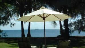 A patio with two chairs and a table under a large umbrella, overlooking a body of water with a sailboat in the distance.