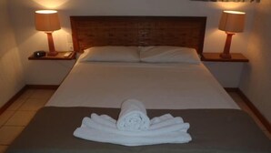 A neatly made bed with a rolled towel in the center, two bedside lamps, and a wooden headboard.