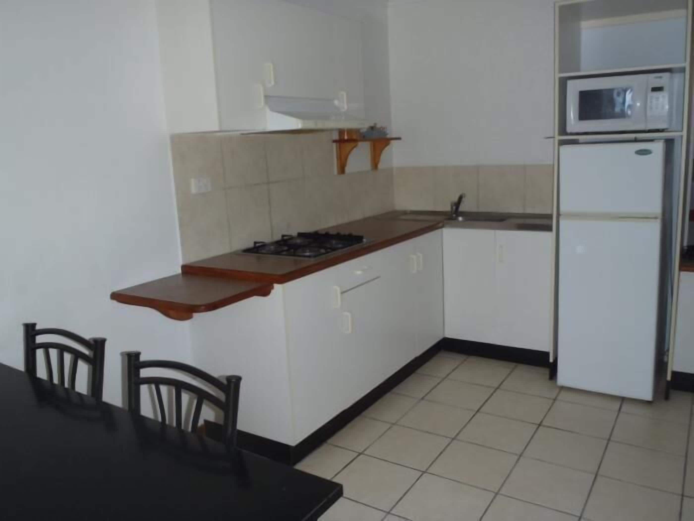 A compact kitchen with a gas stove, a microwave, and a refrigerator. There is a dining table with chairs and a small countertop.