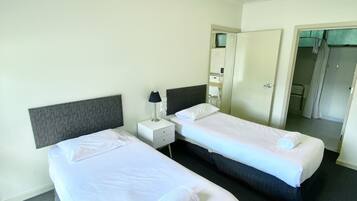 A hotel room with two single beds, a bedside table with a lamp, a mirror, and a door leading to another room.