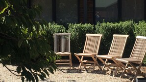 Three wooden lounge chairs arranged in a row on a gravel surface with a hedge and a building in the background. - Ballarat Colonial Motor Inn & Apartments (Warrenheip)
