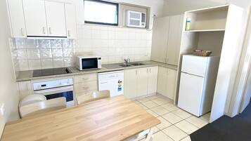 A compact kitchen with white cabinets, a microwave, a dishwasher, and a refrigerator. There is a wooden dining table with chairs.