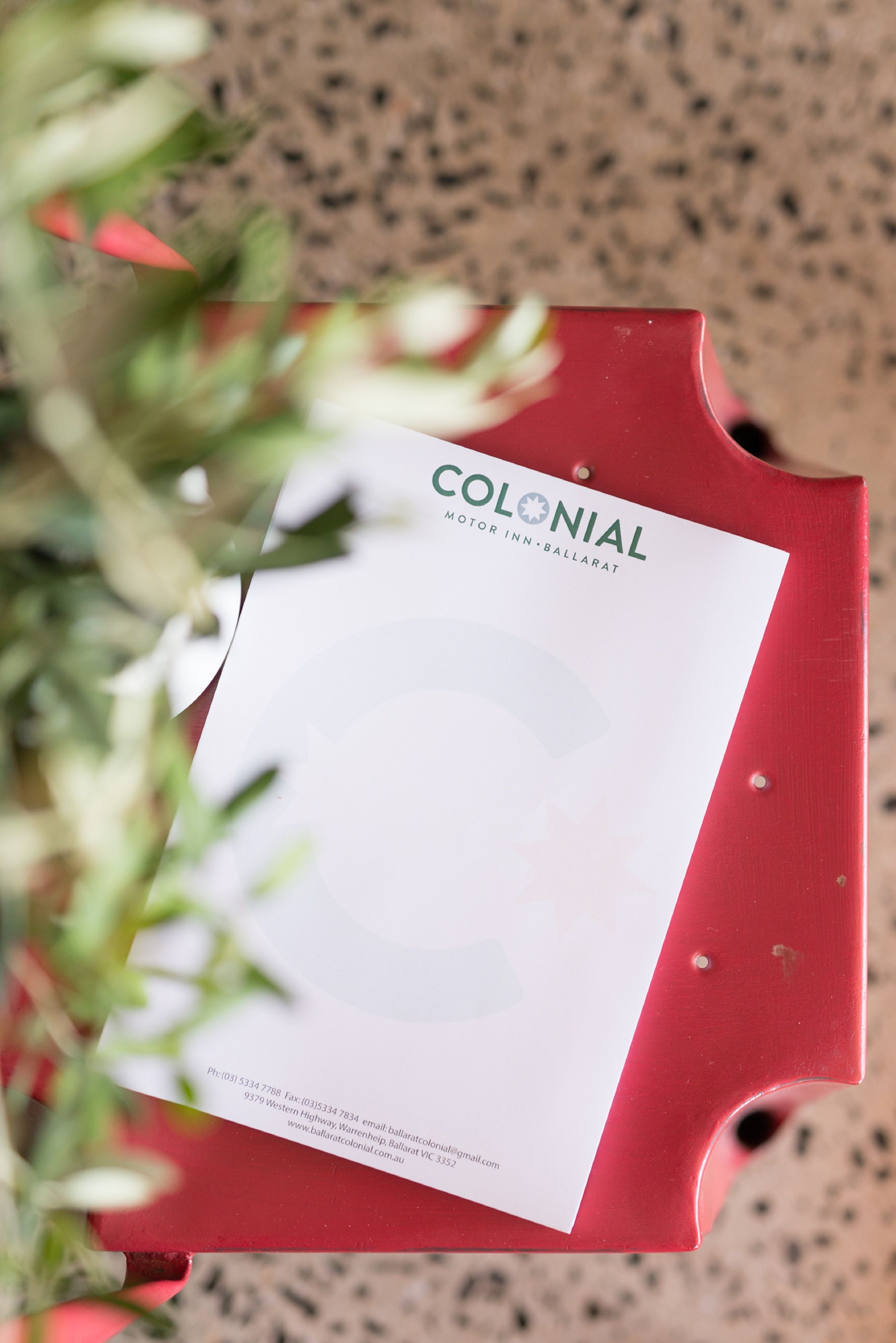 A red folder with a white label that reads "COLONIAL MOTOR INN BALLARAT" along with contact information.