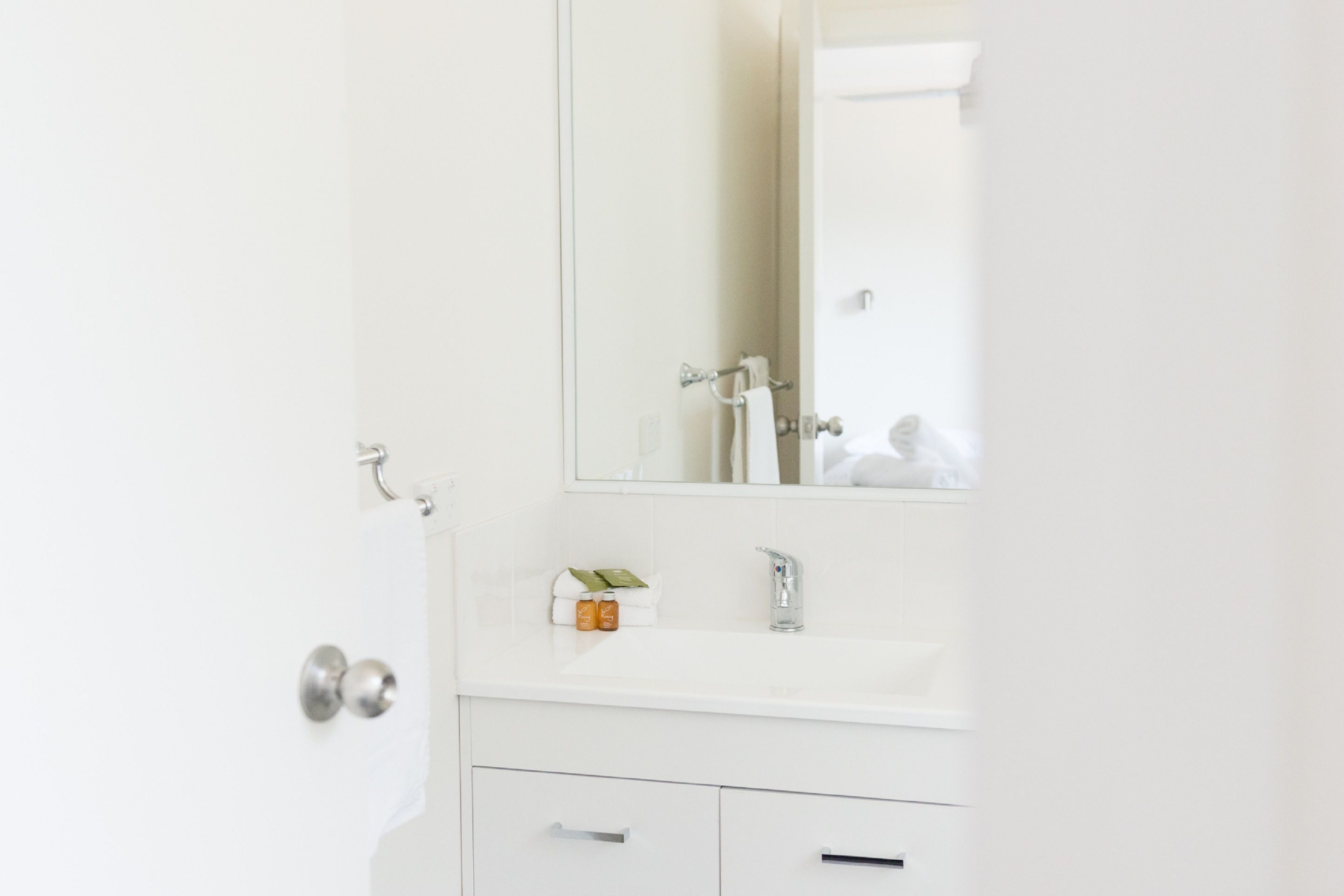 Un baño con un lavamanos blanco, un espejo y una puerta con picaporte plateado.