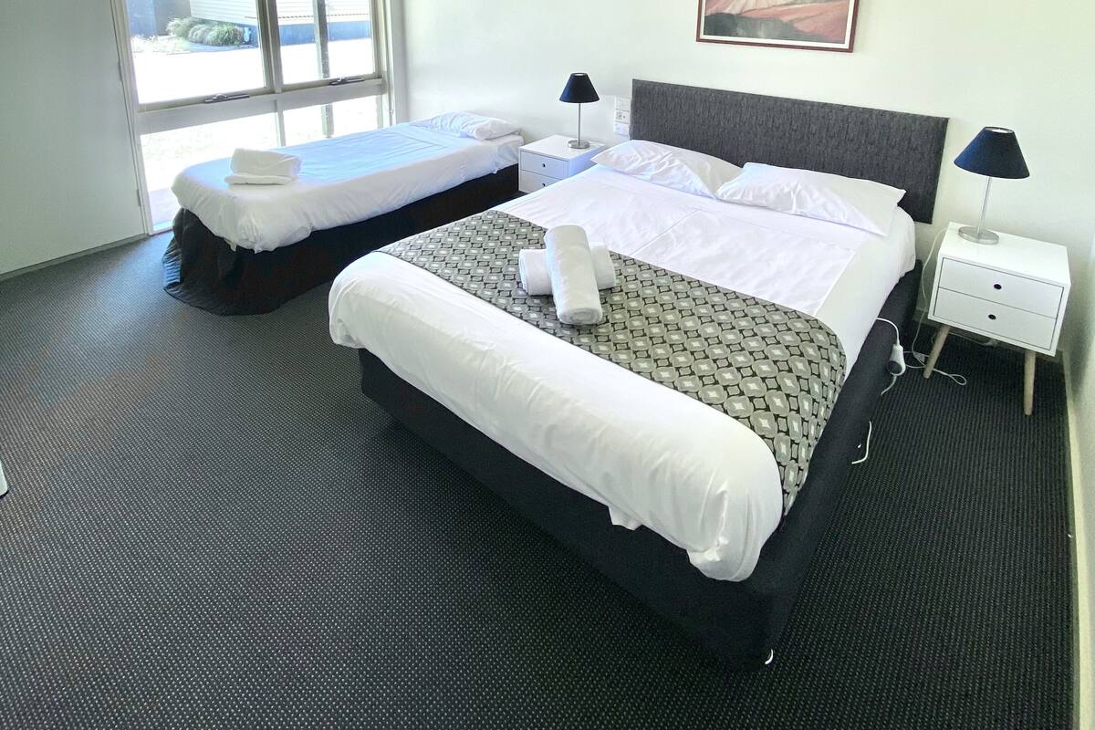 A hotel room with two beds, a large window, a painting on the wall, and a ceiling light.
