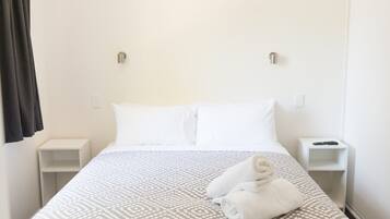 A hotel room with a bed, two bedside tables, and a folded towel on the bed.