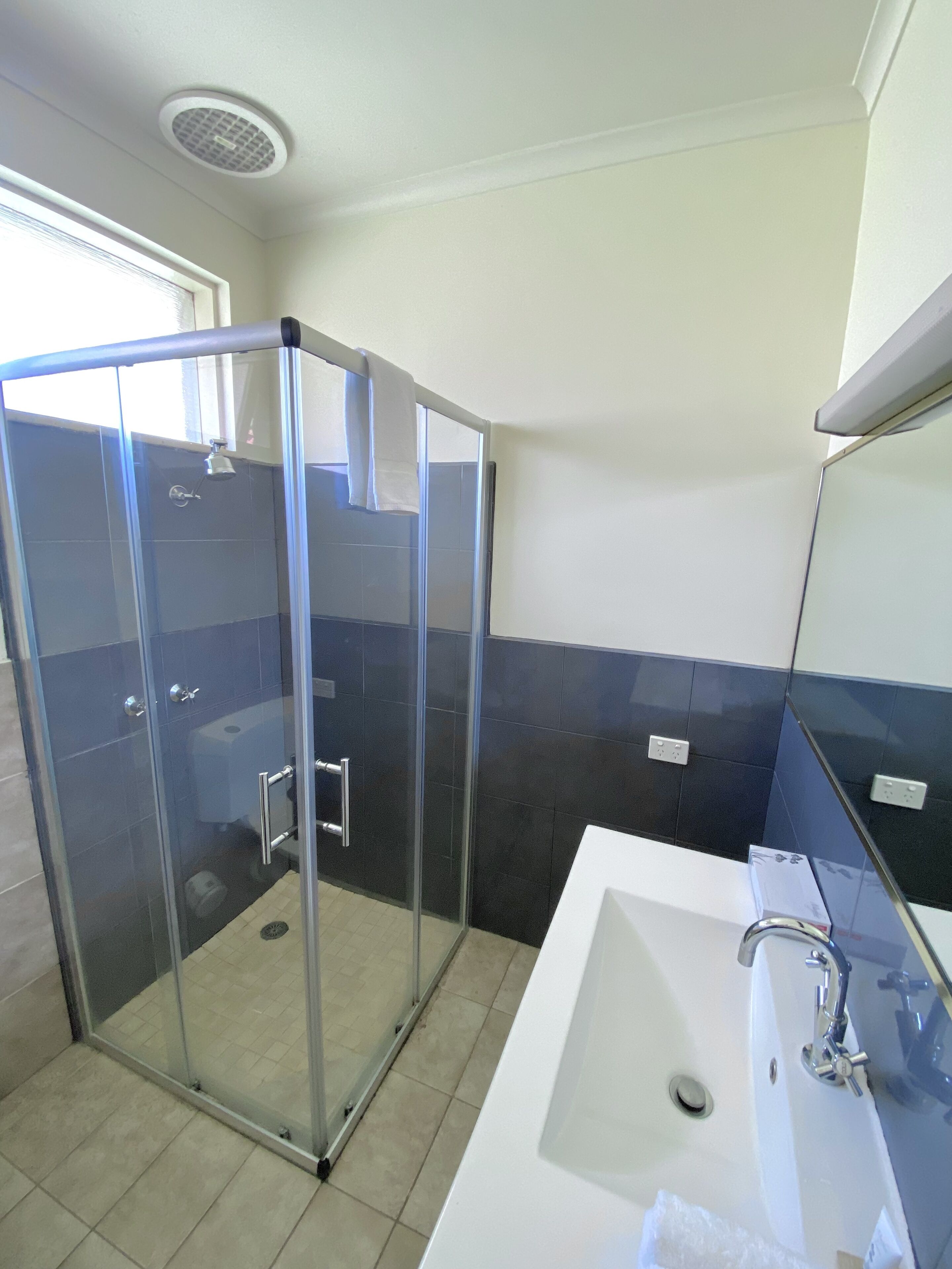 Een moderne badkamer met een douchecabine van glas, een witte wastafel met spiegel en donkerblauwe betegelde wanden.