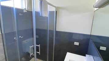 Een moderne badkamer met een douchecabine van glas, een witte wastafel met spiegel en donkerblauwe betegelde wanden.