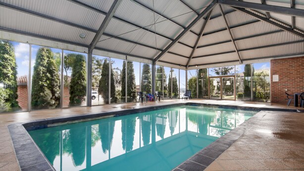 An indoor swimming pool with clear glass walls, a tiled floor, and a metal roof. - Ballarat Colonial Motor Inn & Apartments (Warrenheip)