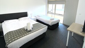 A hotel room with two beds, a desk, a window, and a door. - Ballarat Colonial Motor Inn & Apartments (Warrenheip)