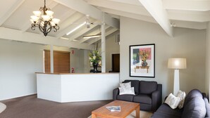 A modern living room with a wooden coffee table, grey sofa, and a white reception desk. - Ballarat Colonial Motor Inn & Apartments (Warrenheip)