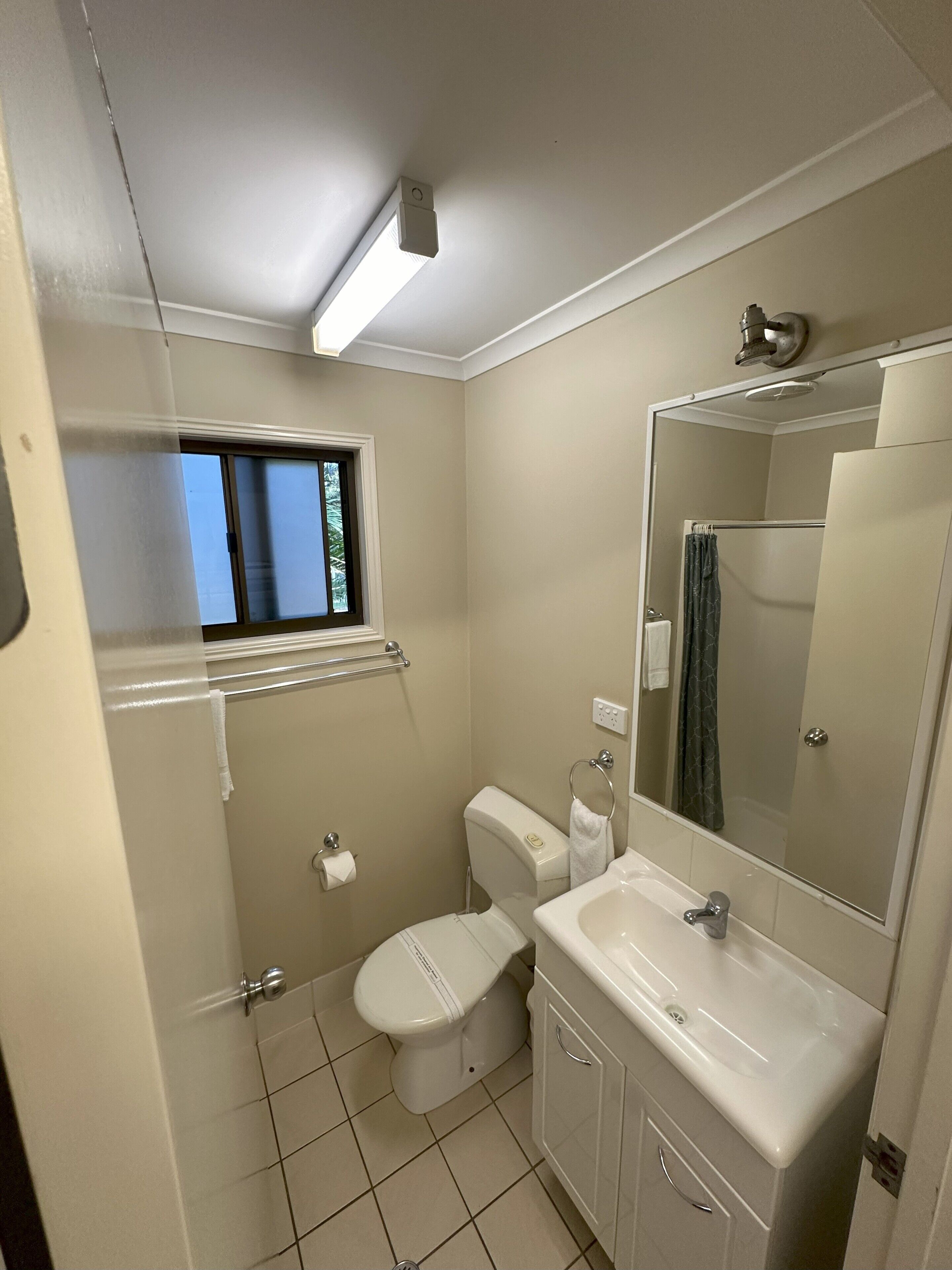 A bathroom with a toilet, sink, mirror, and window.
