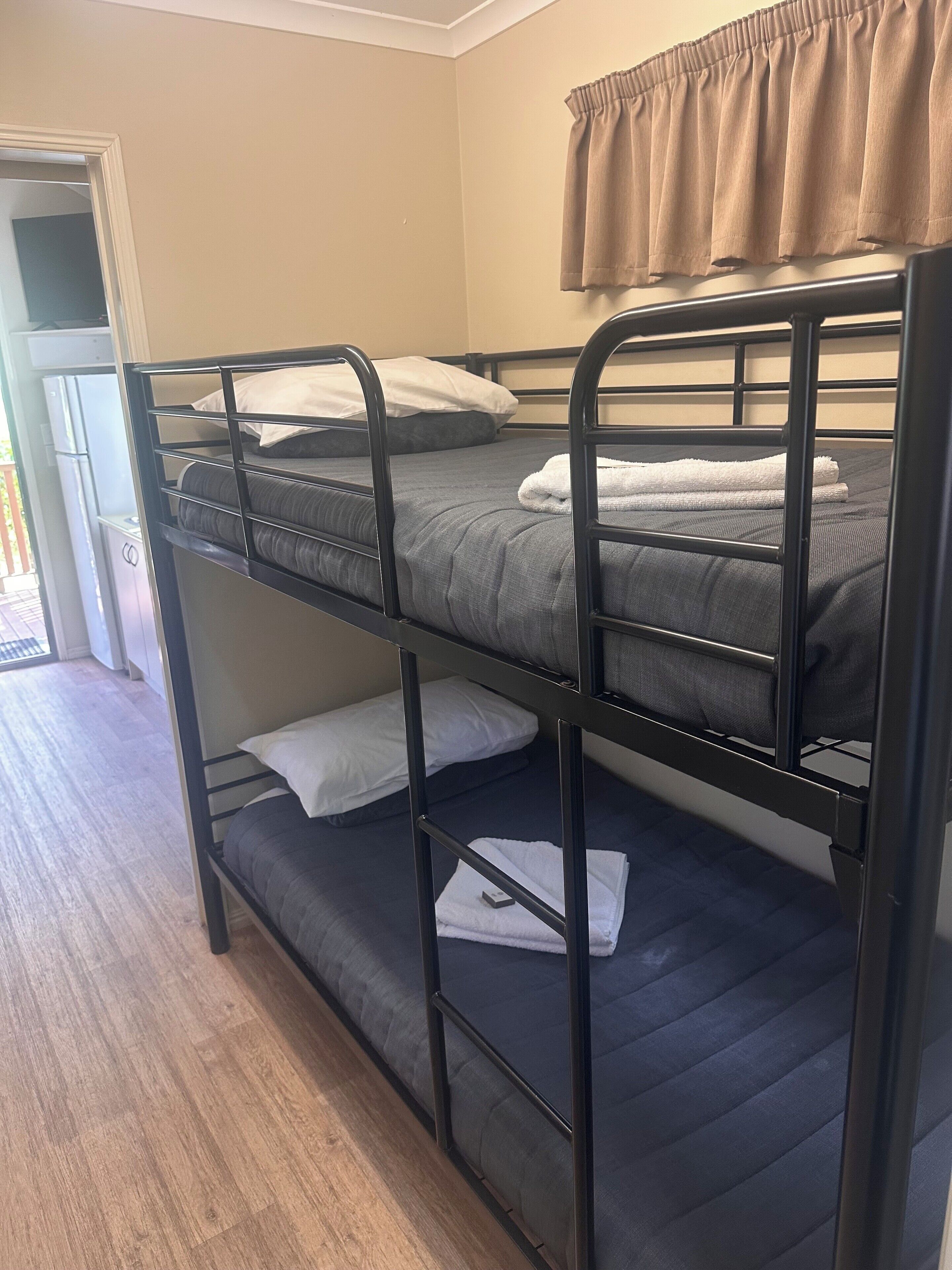 Un lit superposé avec un rideau, un réfrigérateur et un plancher en bois.
