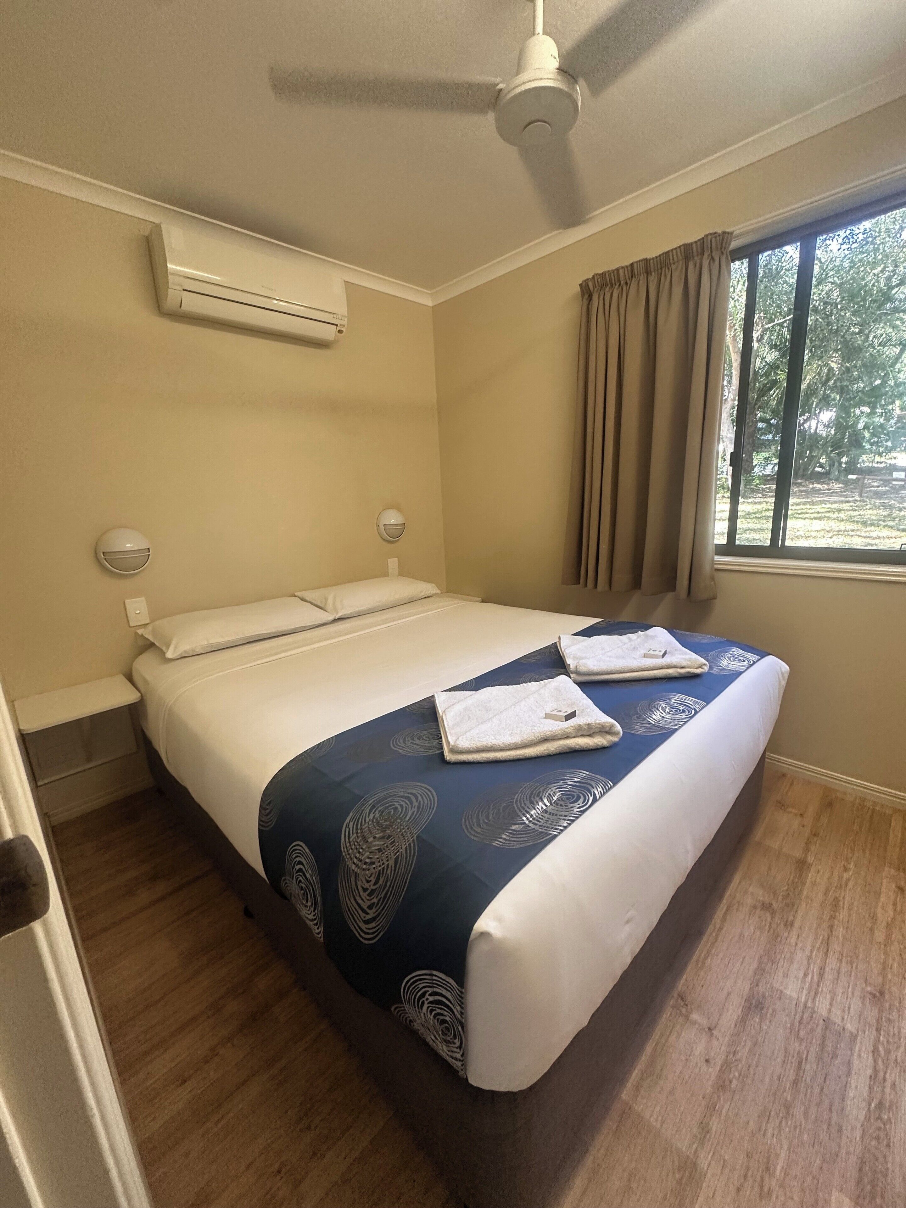 Un dormitorio con cama, aire acondicionado, ventilador de techo, ventana con cortinas y vistas al exterior.