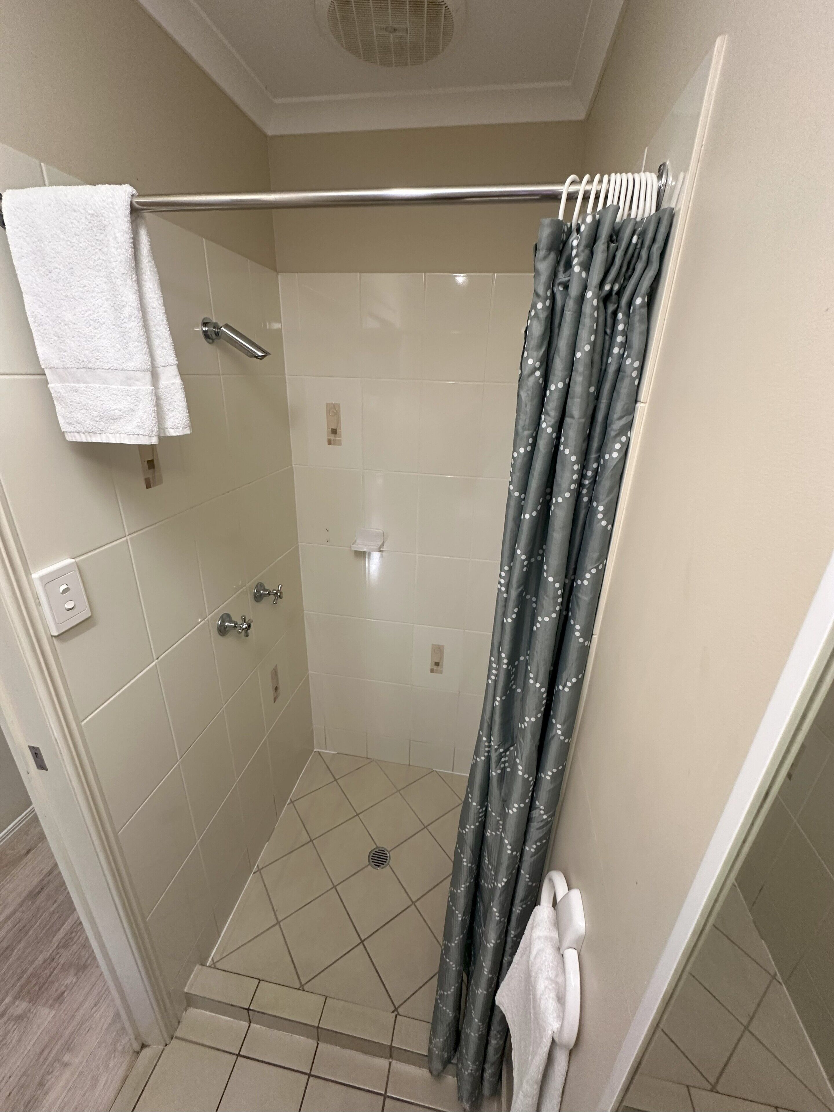 A shower with a grey curtain, a white towel, and a metal shower rod.