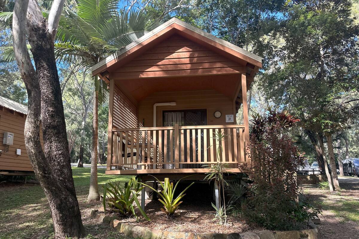 Une cabane en bois dotée d’un balcon, entourée d’arbres et de plantes.