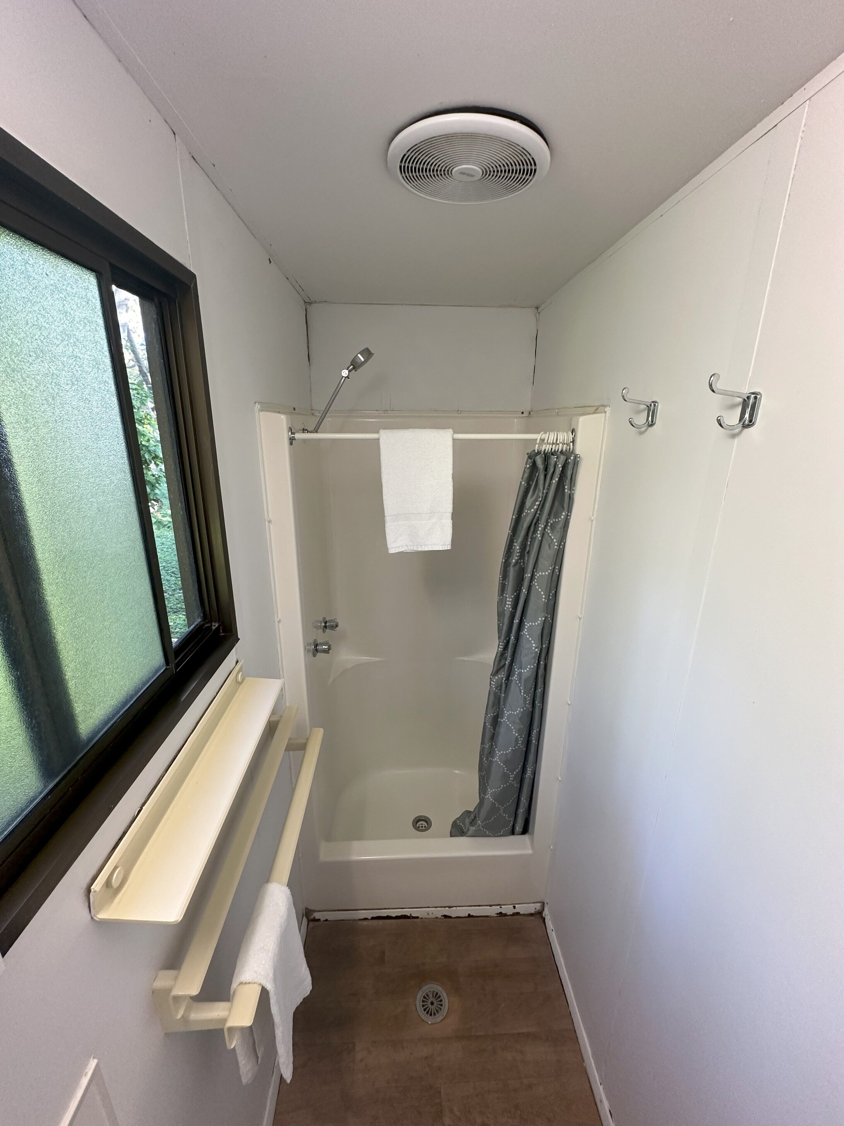 Un piccolo box doccia chiuso, con finestra, portasciùmi e bocchetta di ventilazione a soffitto.