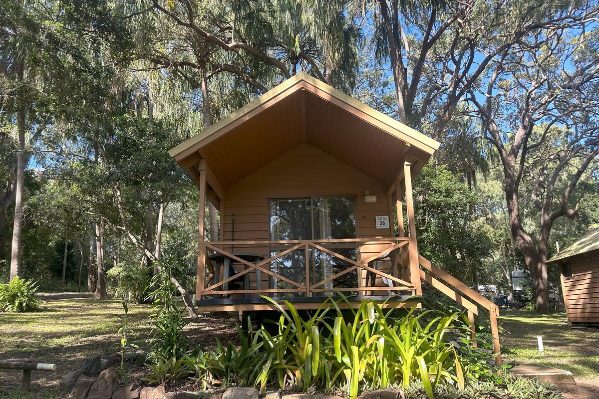 Une cabane en bois dotée d’un balcon, entourée d’arbres et de plantes.