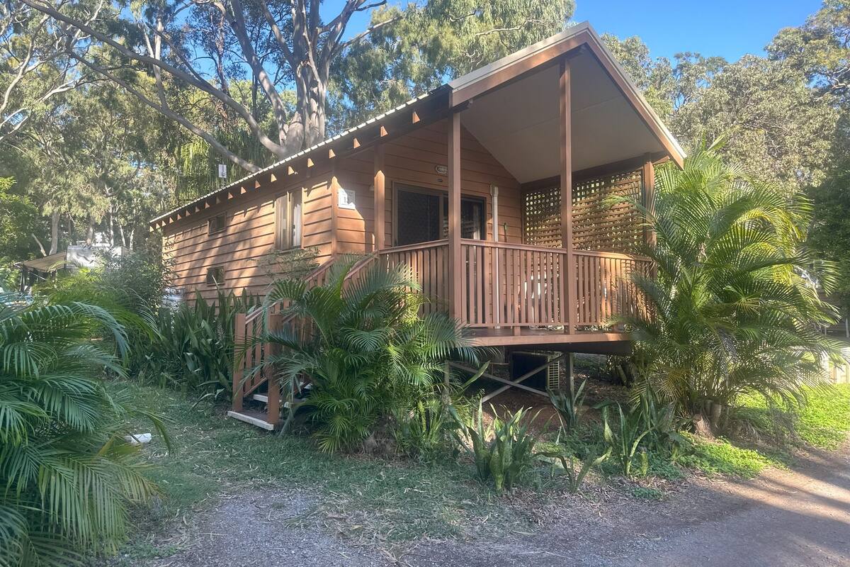 Une cabane en bois dotée d’un balcon, entourée d’une végétation luxuriante et d’arbres.