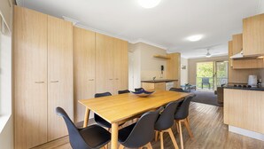 Une cuisine moderne avec des meubles en bois, une table à manger avec des chaises et une vue sur l’extérieur.