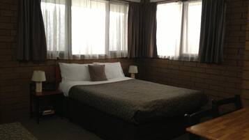 A hotel room with a bed, two bedside tables with lamps, a wooden table, and a brick wall.