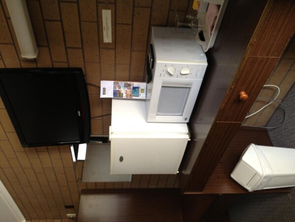 A compact kitchenette with a microwave, a small refrigerator, and a black television.
