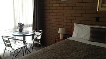 A hotel room with a bed, a round table with chairs, a potted plant, and a window with curtains.