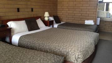 A hotel room with two beds, a nightstand, a lamp, and a brick wall.