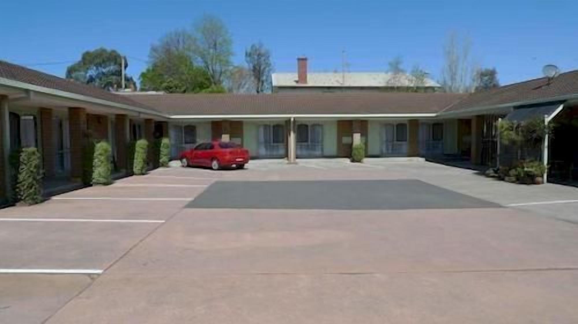 A motel with a central parking area, a red car parked in the lot, and a row of rooms on either side.