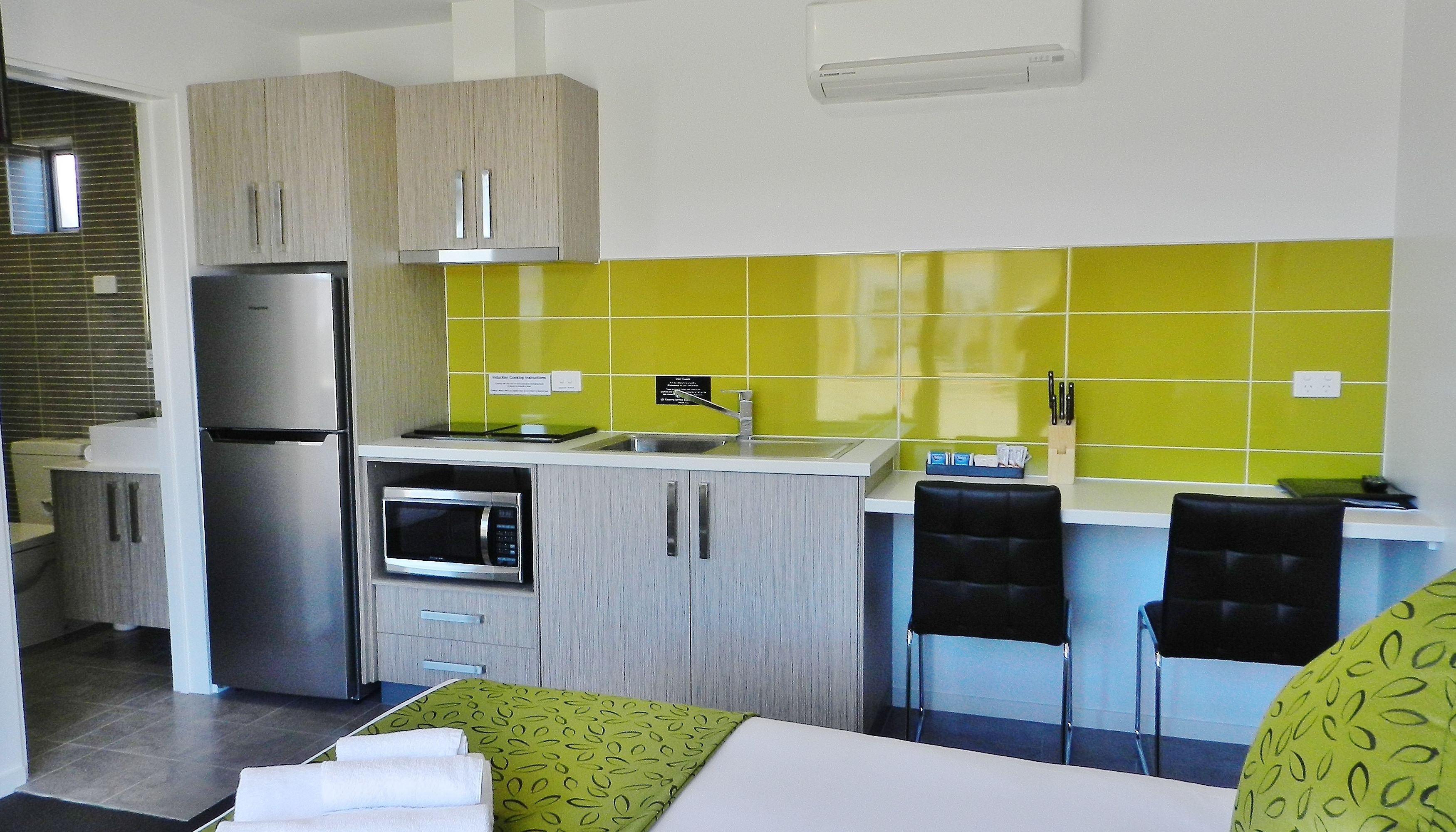 A compact kitchen with a refrigerator, microwave, and sink. There are two black chairs and a small table with a green patterned tablecloth.